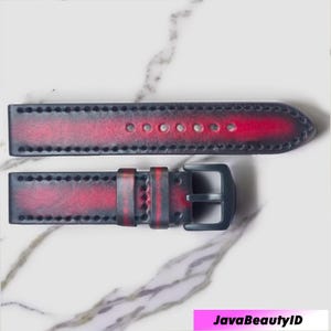 Puede incluir: Una correa de reloj de dos piezas con un diseño degradado. La correa hace la transición de un gris oscuro a un tono rojo vibrante. La correa presenta costuras a lo largo de los bordes y una hebilla gris oscuro.