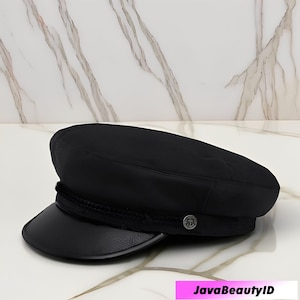 Peut inclure: Un chapeau de marin noir avec une couronne arrondie et un bord court et incurvé. Le chapeau présente un détail de corde tressée autour de la base de la couronne et un petit bouton argenté sur le côté. Le chapeau est en matière lisse et mate.