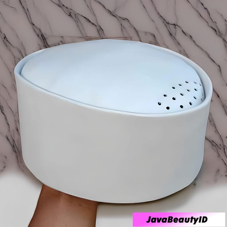 Peut inclure: Un r&eacute;cipient blanc et cylindrique pour produit de beaut&eacute; avec un dessus bleu clair perfor&eacute;. Le r&eacute;cipient a un design arrondi et inclin&eacute; et une finition lisse et mate. Le produit est tenu par une main. Le texte "JavaBeautyID" est en bas.
