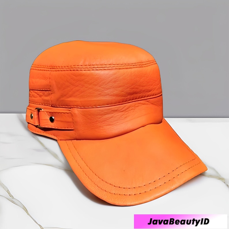 K&ouml;nnte beinhalten: Orangefarbene Lederkappe mit flachem Schirm und strukturierter Krone. Die Kappe hat ein Banddetail mit einer Schnalle an der Seite. Die N&auml;hte sind entlang der N&auml;hte und des Schirms sichtbar. Die Kappe hat eine leuchtende Farbe.