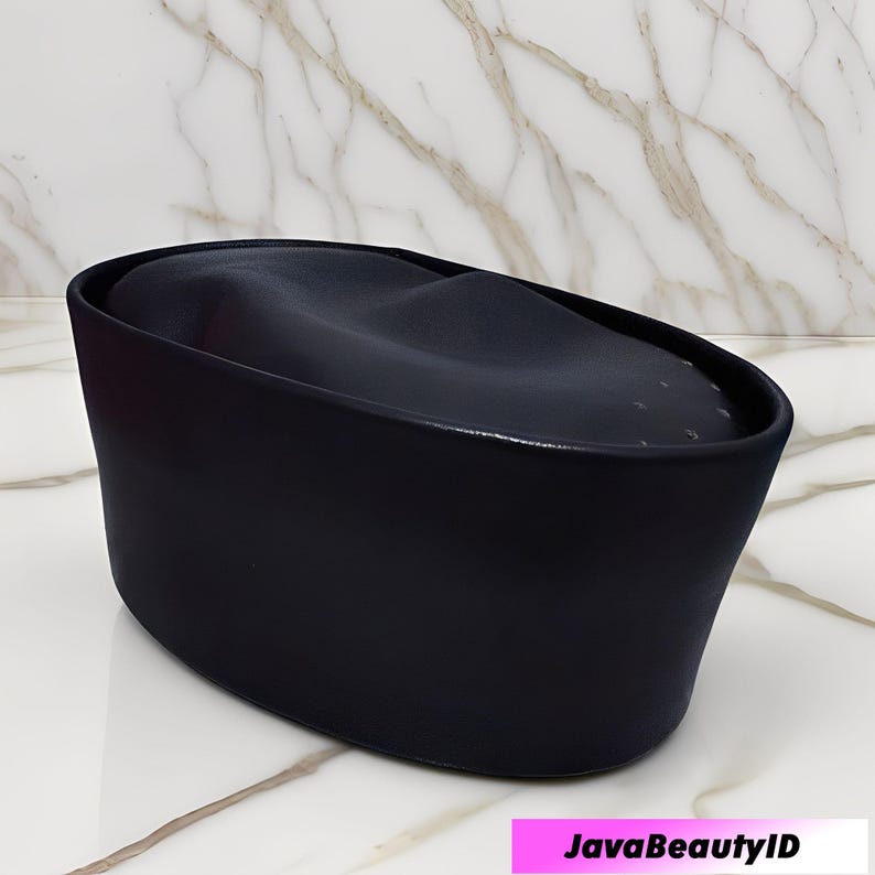 Peut inclure: Un r&eacute;cipient noir de forme ovale pour produits de beaut&eacute;, avec un dessus incurv&eacute;. Le r&eacute;cipient a une finition lisse et mate et repose sur une surface en marbre blanc et gris. Le texte "JavaBeautyID" est affich&eacute; dans un rectangle rose en bas.