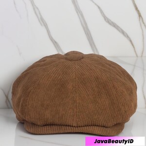 May include: A brown corduroy newsboy cap with a rounded crown and a small, stiff brim. The cap has a textured, ribbed appearance and is made of a soft, durable fabric. The cap is a classic style, suitable for various outfits.
