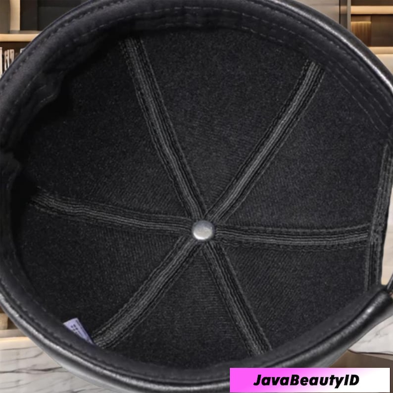 May include: Black cap with a leather brim and a textured fabric crown. The crown is divided into panels with visible stitching, meeting at a central metal button. The interior is lined with a dark fabric.