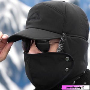 May include: Black winter hat with a built-in face mask and ear flaps. The hat has a curved brim and a logo on the front. The face mask is secured with two buttons. The hat is designed to provide warmth and protection from the cold.