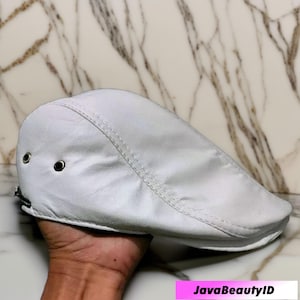 May include: A white leather flat cap with a curved brim. The cap has a stitched seam down the center and two small metal eyelets on the side. The text "JavaBeautyID" is visible in the bottom right corner.