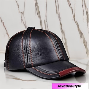 Pode incluir: Boné de beisebol de couro preto com costura vermelha e aba vermelha. O boné tem uma viseira curva e um botão na parte superior. Os detalhes da costura adicionam um elemento decorativo.