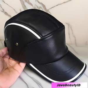 Könnte beinhalten: Schwarze Baseballkappe mit gebogenem Schirm und strukturierter Krone. Die Kappe hat einen weißen Streifen entlang der Oberseite und der Krempenkanten. Hergestellt aus einem glatten Material, hat sie ein klassisches, sportliches Design.