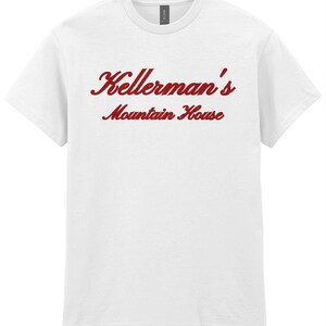 Op de afbeelding: Wit T-shirt met de rode tekst "Kellerman's Mountain House" in een sierlijk lettertype. Het shirt met korte mouwen en ronde hals is gemaakt van een zacht materiaal. Het Gildan-merkteken is zichtbaar bij de halslijn.