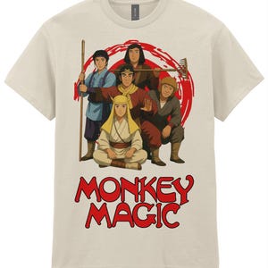May include: A beige short-sleeved t-shirt featuring a graphic illustration of five characters from Monkey Magic. The design includes a red circular background and the text MONKEY MAGIC in bold red letters at the bottom of the shirt front.