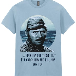 Op de afbeelding: Lichtblauw T-shirt met een zwart-wit afbeelding van een man met een pet, tegen een zeebodem. Het shirt bevat de tekst: "I'LL FIND HIM FOR THREE, BUT I'LL CATCH HIM AND KILL HIM FOR TEN."