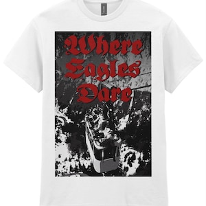 May include: A white short-sleeve t-shirt featuring a rectangular graphic print on the chest. The graphic depicts a black and white scene of a cable car suspended over a mountainous landscape, with the red text Where Eagles Dare printed above.