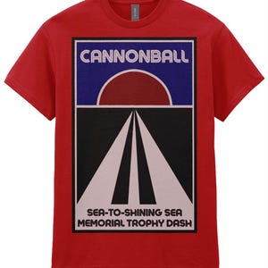 Può includere: T-shirt rossa con un design grafico con la scritta "CANNONBALL" sopra un sole rosso e un disegno stradale. Sotto il disegno stradale c'è il testo "SEA-TO-SHINING SEA MEMORIAL TROPHY DASH."