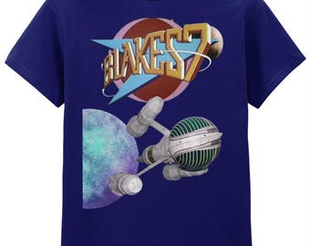 Op de afbeelding: Marineblauw t-shirt met een grafisch ontwerp. Het ontwerp bevat de tekst "BLAKES 7" in goud en wit, tegen een roze en bruine cirkelvormige achtergrond. Een ruimteschip en een planeet zijn ook afgebeeld.