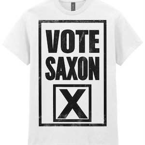 Op de afbeelding: Wit t-shirt met een zwarte opdruk. De opdruk toont de woorden "VOTE SAXON" in een rechthoekige kader en een grote "X" in een vak eronder. Het ontwerp heeft een vintage uitstraling.
