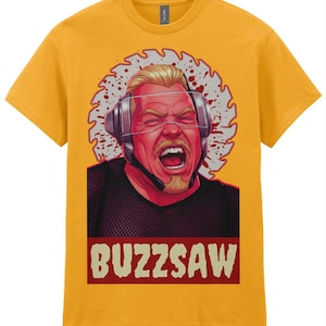 May include: A mustard yellow short-sleeve t-shirt featuring a graphic print of a person wearing a headset with a buzzsaw blade background. The person has a shouting expression and is wearing a black mesh top. The text BUZZSAW is printed below.