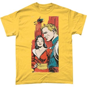 May include: Mustard yellow t-shirt with a retro comic book design. The print shows a man and woman in vintage clothing, with a futuristic city and a flying craft in the background. The artwork is in a classic comic book style.