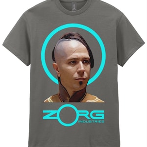 May include: Grey t-shirt with a portrait of a man with a shaved head and a teal circle. The text "ZORG INDUSTRIES" is below the portrait in teal. The shirt is a Gildan brand.