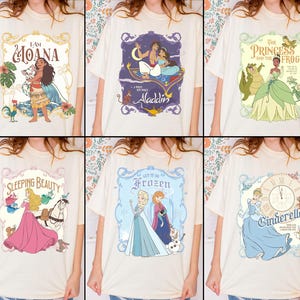 May include: Cream-colored t-shirts featuring various Disney movie graphics. Designs include "I Am Moana," "Aladdin," "The Princess and the Frog," "Sleeping Beauty," "Frozen," and "Cinderella." Each graphic is framed with decorative borders and vibrant colors.