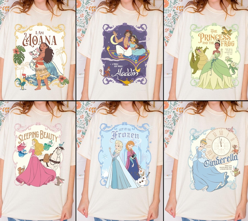 May include: Cream-colored t-shirts featuring various Disney movie graphics. Designs include "I Am Moana," "Aladdin," "The Princess and the Frog," "Sleeping Beauty," "Frozen," and "Cinderella." Each graphic is framed with decorative borders and vibrant colors.