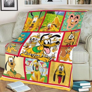 May include: A yellow and red throw blanket featuring a collage of Pluto cartoon images. The blanket has a yellow border and a grid pattern with various Pluto illustrations, including the text "Custom Name". The blanket is draped over a light-colored sofa.