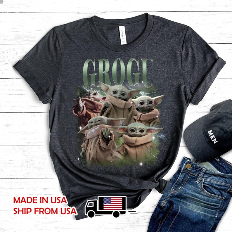 May include: A dark charcoal gray short-sleeve t-shirt featuring a graphic print of five Grogu characters in tan robes. The text GROGU is printed in large, light green letters above the characters. The design includes subtle lightning and star accents.