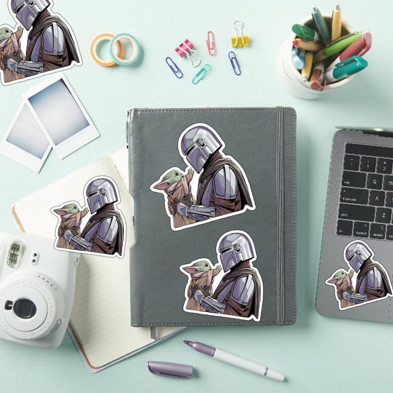 May include: A collection of stickers featuring a character in silver armor holding a small green creature. The stickers are in various sizes and are placed on a gray notebook, a laptop, and a white instant camera. Other office supplies are also visible.