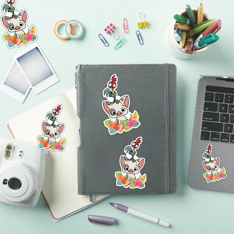 May include: A collection of colorful stickers featuring a cartoon pig character with a rooster on its head, surrounded by flowers. The stickers are placed on a gray notebook, a laptop, and a white camera, with stationery items scattered around.