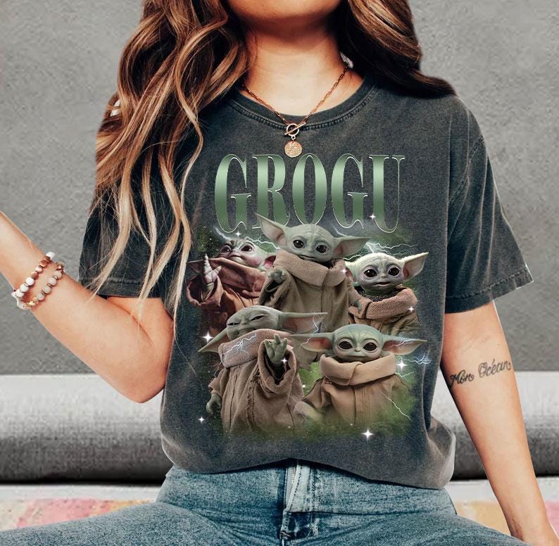 May include: A charcoal gray short-sleeve t-shirt featuring a graphic print of multiple Grogu characters in tan robes. The text GROGU is printed in large green letters above the characters, with green lightning accents surrounding the figures.