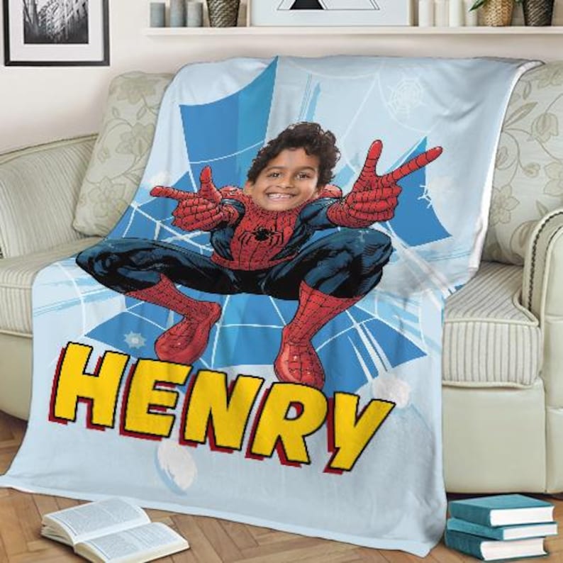 Op de afbeelding: Een lichtblauwe deken met een gepersonaliseerd Spider-Man-ontwerp met de naam "HENRY" in gele letters. De deken toont het gezicht van een kind dat is overgelegd op het Spider-Man-personage, met een webpatroon.