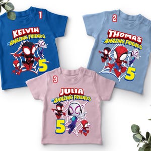 May include: Three children's t-shirts in blue, light blue, and pink. Each shirt features a graphic of Spider-Man and friends, a name, and the number 5. The text on the shirts reads "Kelvin & Amazing Friends", "Thomas & Amazing Friends", and "Julia & Amazing Friends".