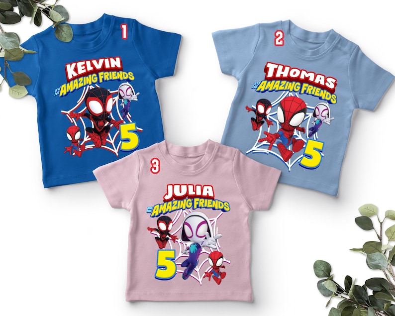 May include: Three children's t-shirts in blue, light blue, and pink. Each shirt features a graphic of Spider-Man and friends, a name, and the number 5. The text on the shirts reads "Kelvin & Amazing Friends", "Thomas & Amazing Friends", and "Julia & Amazing Friends".