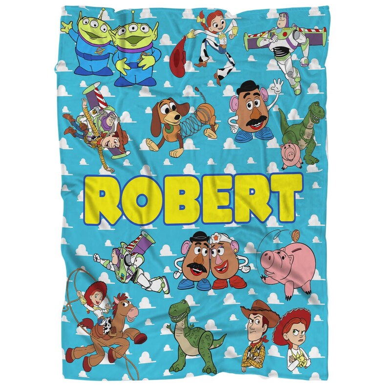 K&ouml;nnte beinhalten: Eine blaue Decke mit Figuren aus dem Film Toy Story. Die Decke hat einen hellblauen Hintergrund mit wei&szlig;en Wolken und dem Namen "ROBERT" in Gelb. Verschiedene Zeichentrickfiguren sind abgebildet.