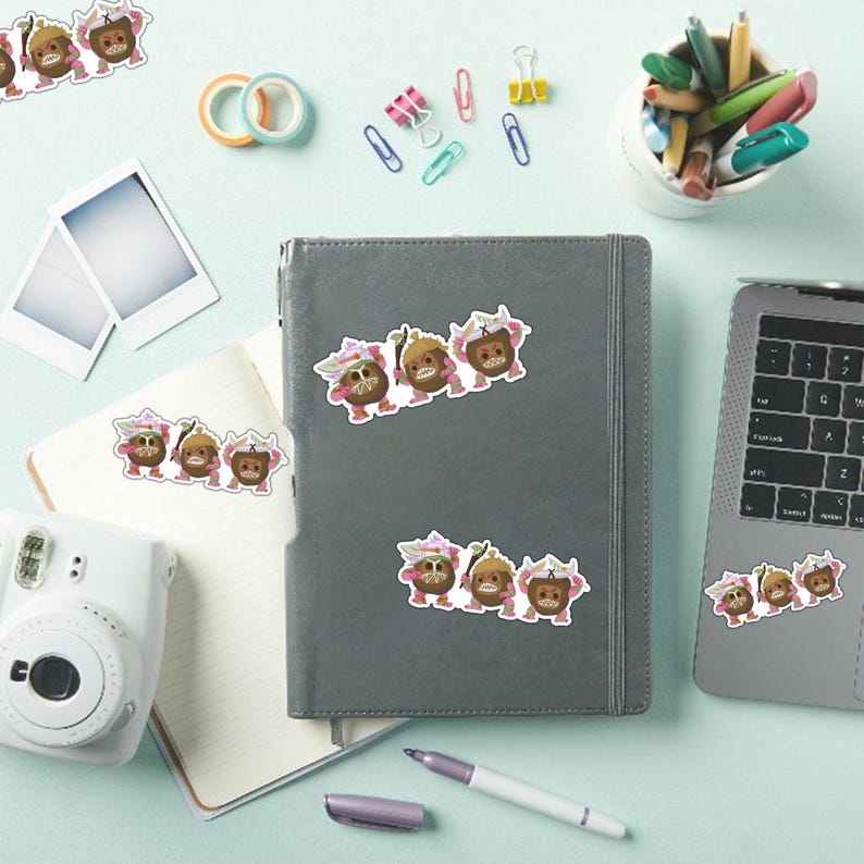 Op de afbeelding: Stickers met cartoon eikel-personages met roze bloemenaccenten. De stickers zijn geplaatst op een grijze notebook, een laptop en een witte camera. Kantoorartikelen zoals pennen, paperclips en tape zijn ook zichtbaar.