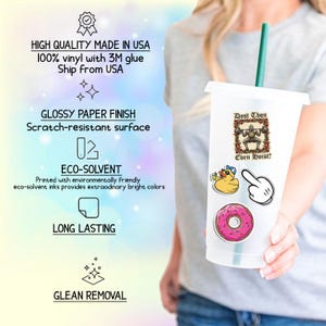 May include: A clear plastic tumbler with a green straw, decorated with various stickers. Stickers include a cartoon duck, a pointing hand, a pink donut, and a weightlifting robot with the text "Dost Thou Even Hoist?"
