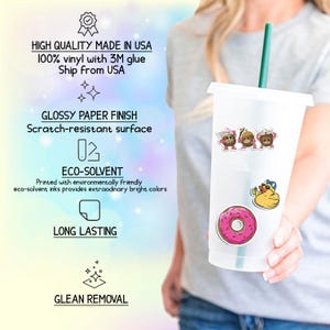 Op de afbeelding: Een doorzichtige plastic beker met een groen rietje, versierd met kleurrijke stickers. De stickers bevatten cartoonfiguren en een roze donut. De tekst op de afbeelding luidt "HIGH QUALITY MADE IN USA".