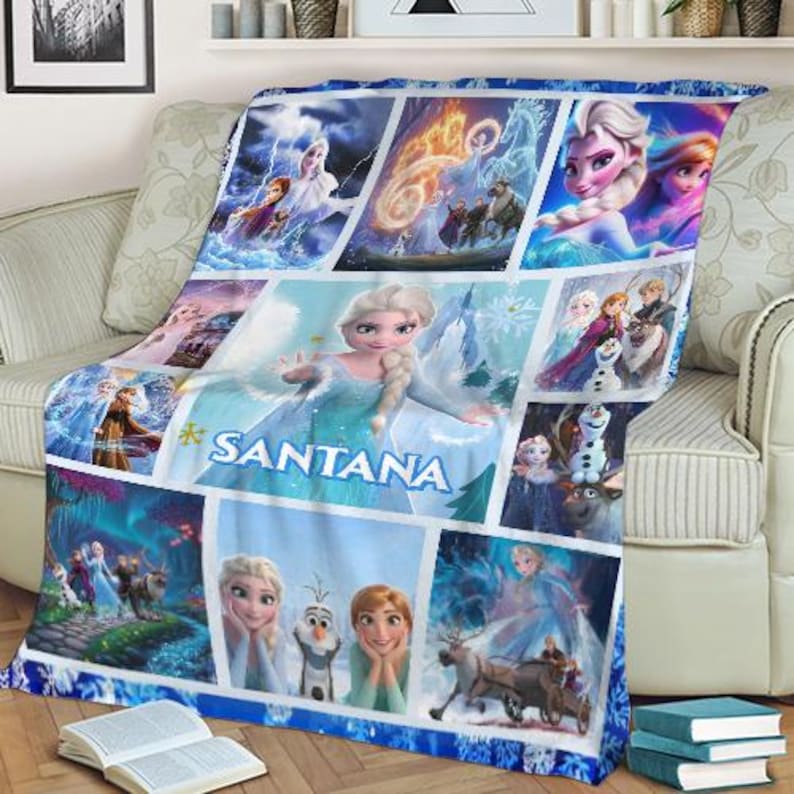 May include: A blue and white fleece blanket featuring a collage of images from the animated film Frozen. The blanket has a personalized name, "SANTANA", and includes images of Elsa, Anna, Olaf, and Kristoff. The blanket is draped over a beige sofa.
