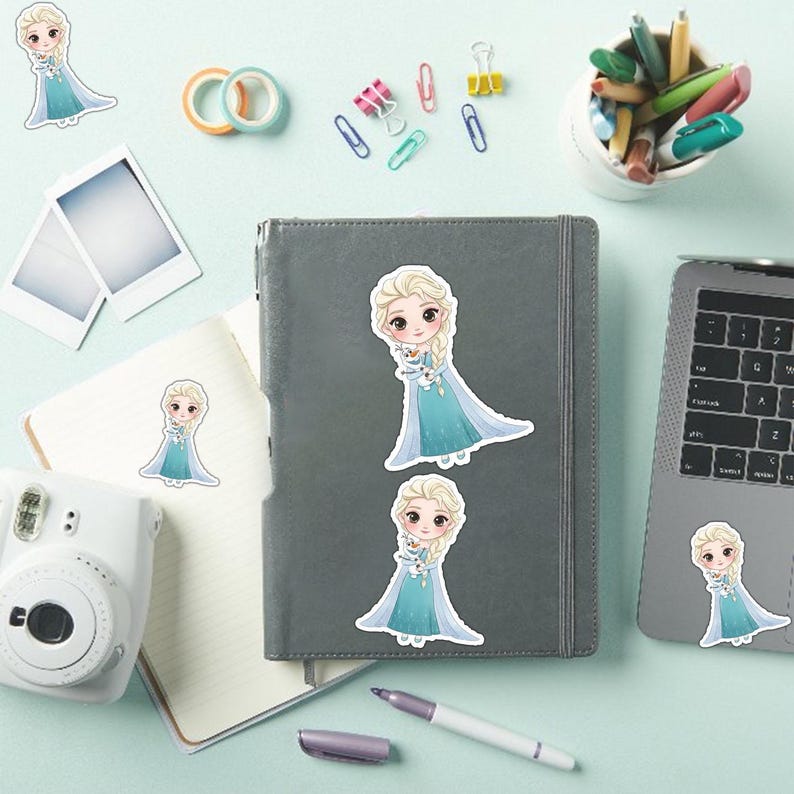 May include: Sticker set featuring a cartoon character in a blue dress with blonde hair. The stickers are placed on a gray notebook, a laptop, and a white camera. Other stationery items, such as pens and paperclips, are also visible.