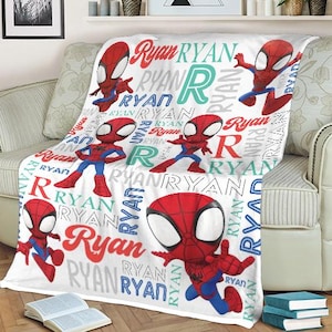 May include: White blanket featuring a repeating pattern of the name "Ryan" in various colors and fonts, along with cartoon illustrations of a superhero in a red and blue suit. The blanket is draped over a sofa.
