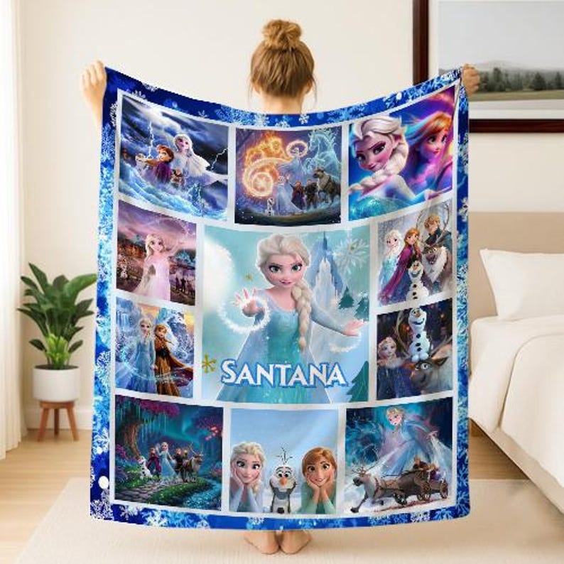 May include: A blue and white fleece blanket featuring multiple images of characters from the animated film "Frozen." The blanket has a central image of Elsa with the name "SANTANA" and a snowflake border.