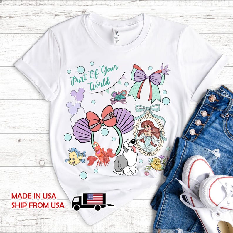 May include: A white t-shirt featuring a graphic print with the text Part Of Your World, a pair of purple seashell ears with a pink bow, a portrait of a red-haired character, a crab, a yellow fish, a white and grey dog, and a large bow.