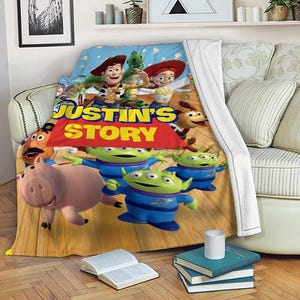May include: A colorful blanket featuring characters from the animated movie "Toy Story." The blanket displays Woody, Rex, Jessie, and the Little Green Men, with the text "JUSTIN'S STORY" in large yellow letters on a red banner.