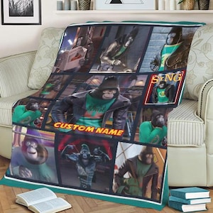 May include: A plush blanket featuring a collage of images of a gorilla character from the movie "Sing". The design includes the text "CUSTOM NAME" and "SING". The blanket has a teal border and is draped over a beige sofa.