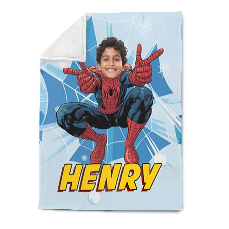 Op de afbeelding: Een lichtblauwe deken met een gepersonaliseerd Spider-Man-ontwerp. De deken heeft een witte sherpa fleece achterkant. Het ontwerp bevat het gezicht van een kind ge&iuml;ntegreerd in het Spider-Man-kostuum, met de naam "HENRY" in gele en rode blokletters.
