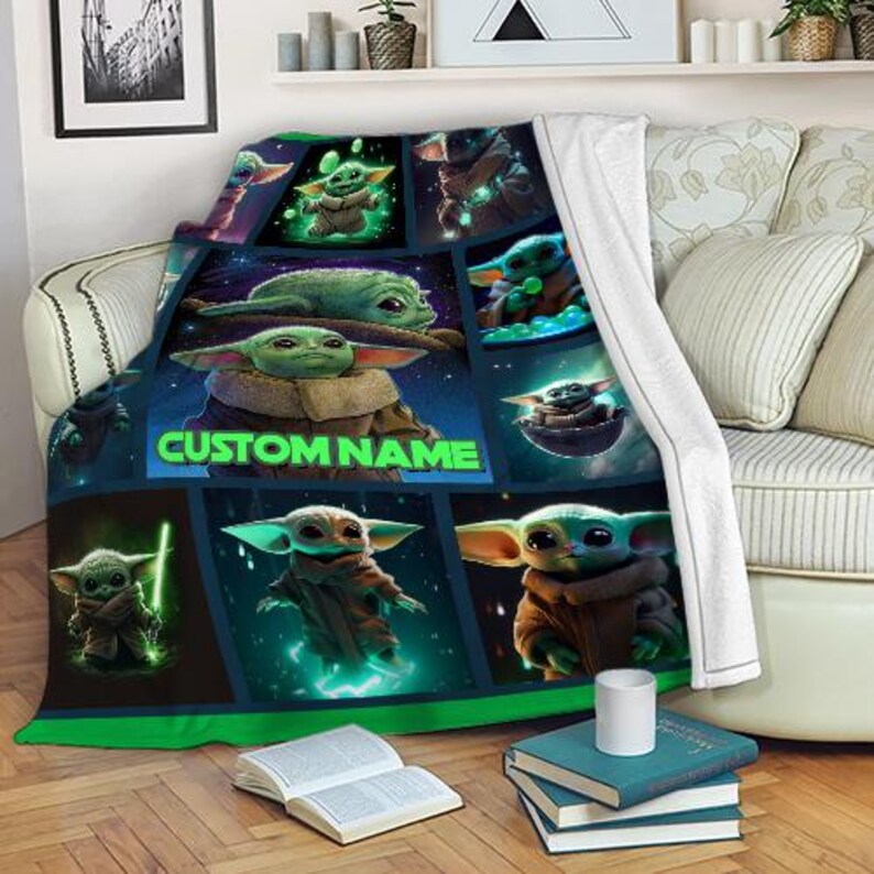 K&ouml;nnte beinhalten: Eine dunkelblaue Decke mit einem Rastermuster, das verschiedene Bilder einer gr&uuml;nen Alien-Figur zeigt. Die Decke tr&auml;gt den Text "CUSTOM NAME" in Gr&uuml;n. Sie ist &uuml;ber ein Sofa drapiert.