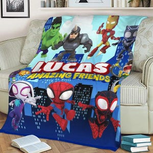 May include: A blue blanket featuring various superhero characters, including Spider-Man and the Hulk, with the text "LUCAS AMAZING FRIENDS" in large, white letters. The blanket is draped over a sofa, showcasing a cityscape design.