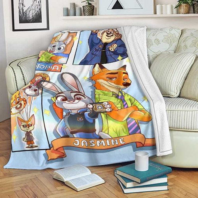 Pode incluir: Um cobertor azul claro e branco com personagens de desenhos animados de Zootopia. O cobertor tem uma borda azul clara e um design central com Judy Hopps, Nick Wilde e outros personagens. O nome "Jasmine" est&aacute; escrito em uma faixa laranja.