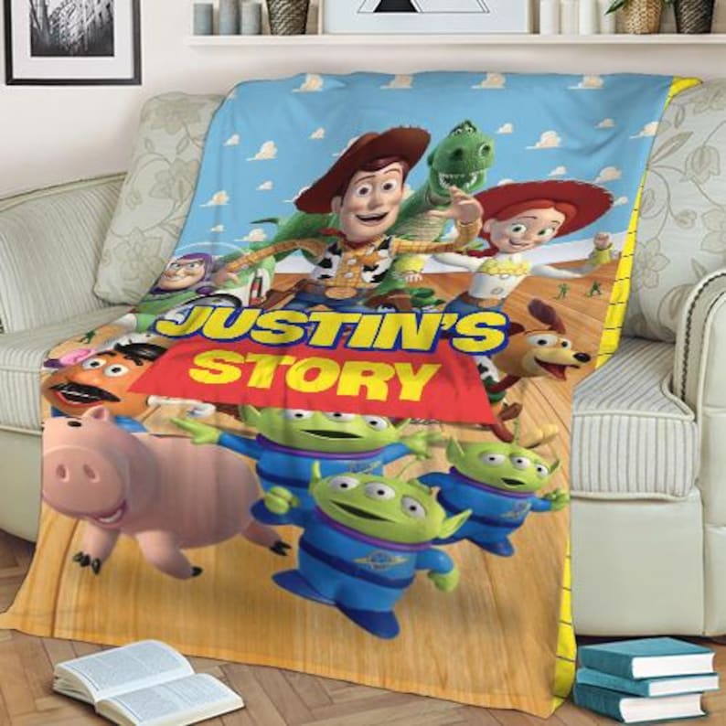 May include: A plush blanket featuring characters from the animated film Toy Story. The blanket displays Woody, Rex, Jessie, and other characters against a blue sky background. The text "JUSTIN'S STORY" is prominently displayed.