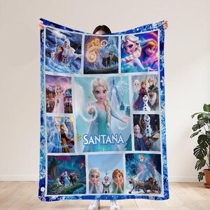 May include: A blue fleece blanket featuring multiple images of Elsa from the movie Frozen. The blanket has a collage design with a snowflake border and the name "SANTANA" in the center.
