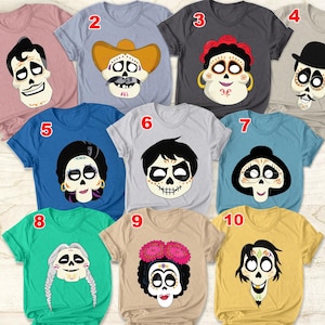Könnte beinhalten: Eine Sammlung von zehn kurzärmeligen T-Shirts, jedes mit einem einzigartigen Sugar-Skull-Design. Die Shirts sind in verschiedenen Farben erhältlich, darunter Rosa, Blau, Grau und Grün. Die Sugar-Skull-Designs haben unterschiedliche Frisuren, Hüte und florale Akzente.