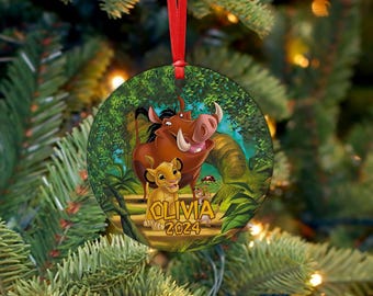 May include: Round Christmas ornament featuring characters from The Lion King. The ornament has a red ribbon for hanging. The design includes Simba, Pumbaa, and Timon, with the name "Olivia" and the year "2024" printed on it.